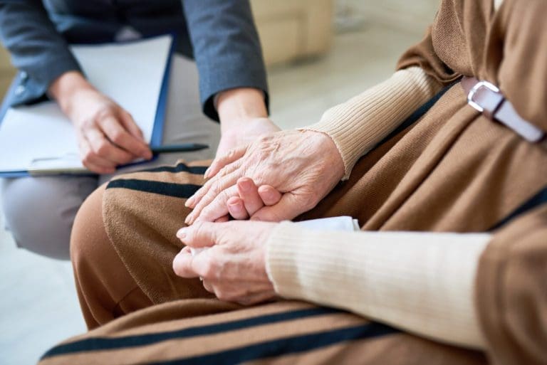 Person with a clipboard holder the hand of an elderly woman. Image for Older Adult Services